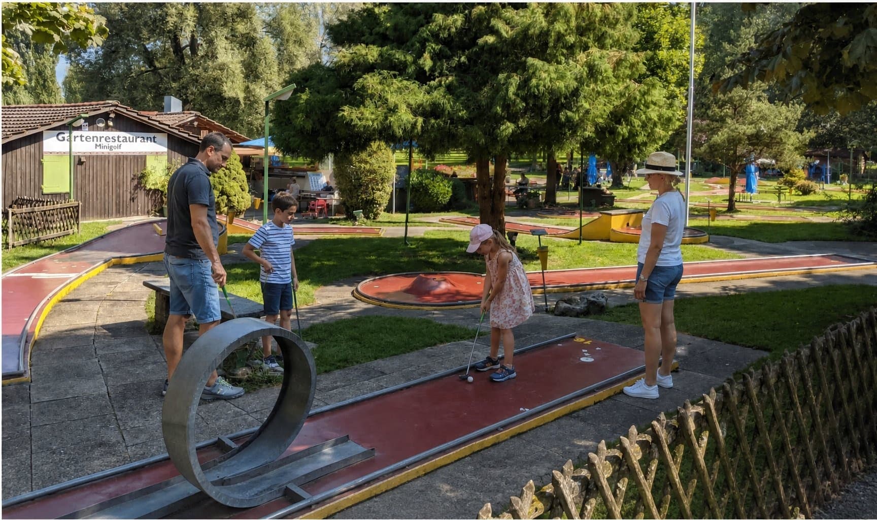 Familie spielt Minigolf auf einer Bahn mit Looping-Hindernis im Sommer.